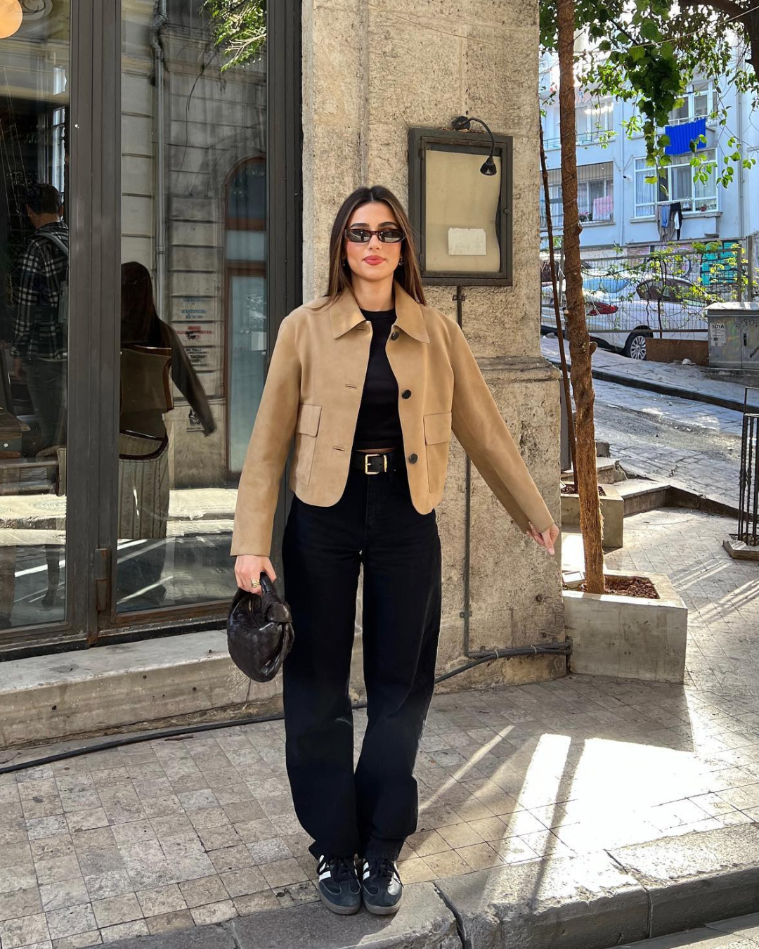 Woman in a beige jacket and black pants standing on a city street.