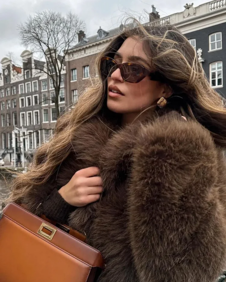 Woman wearing a fur coat and sunglasses with a cityscape background