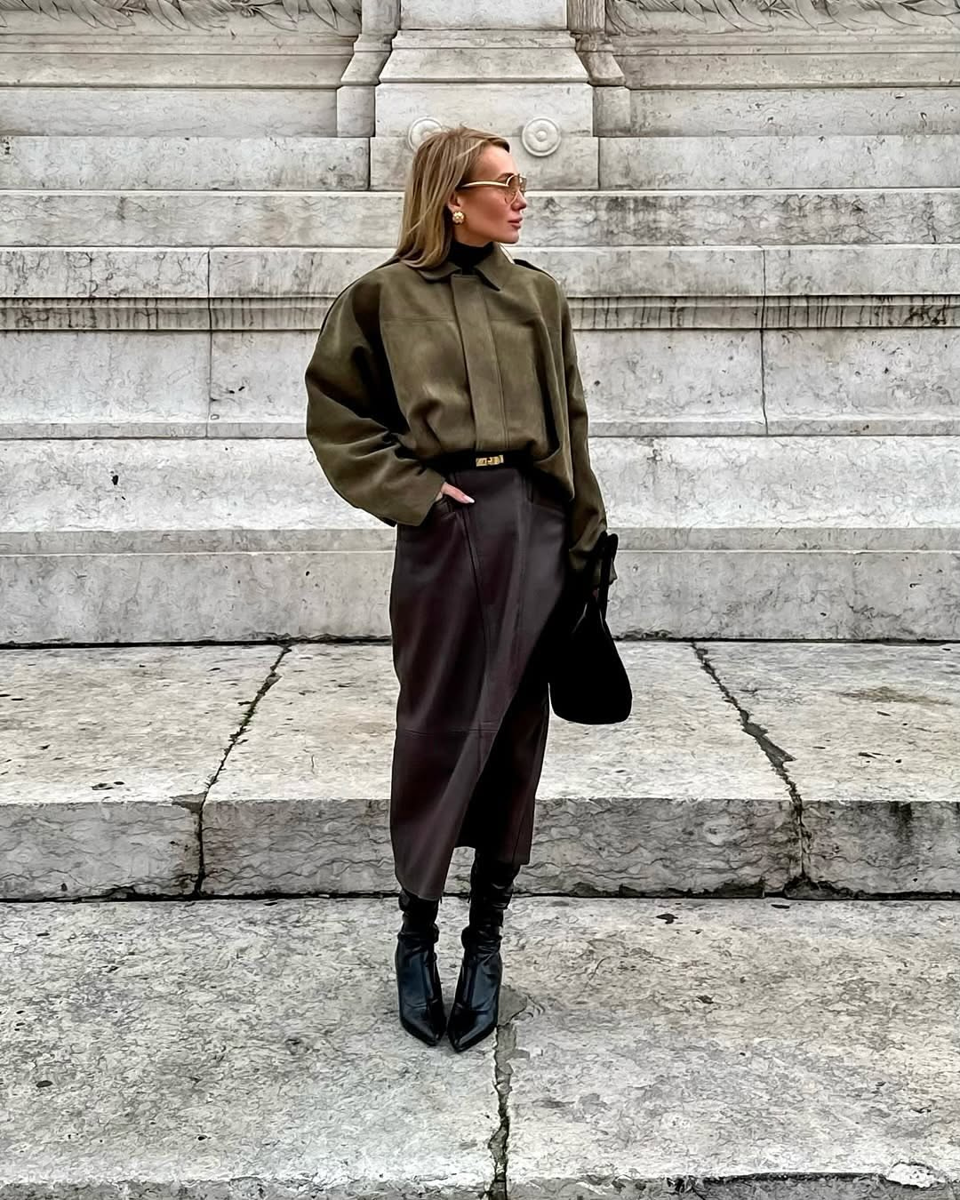 Person wearing a green sweater and brown skirt standing on stone steps.