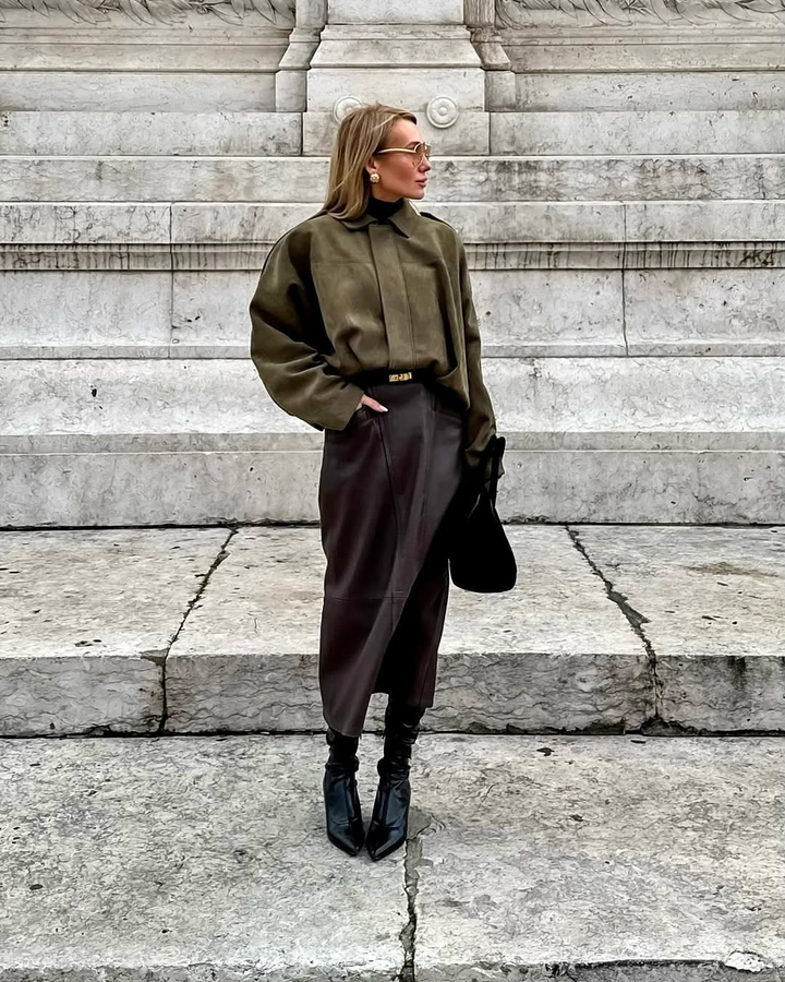 Person wearing a green sweater and brown skirt standing on stone steps.