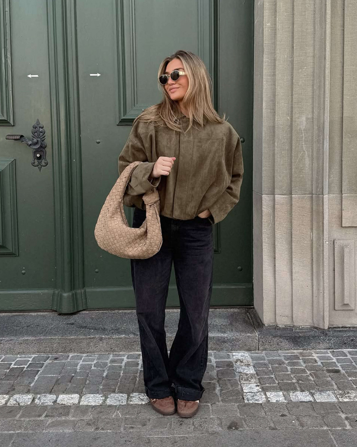 Woman holding a beige handbag in front of a green door