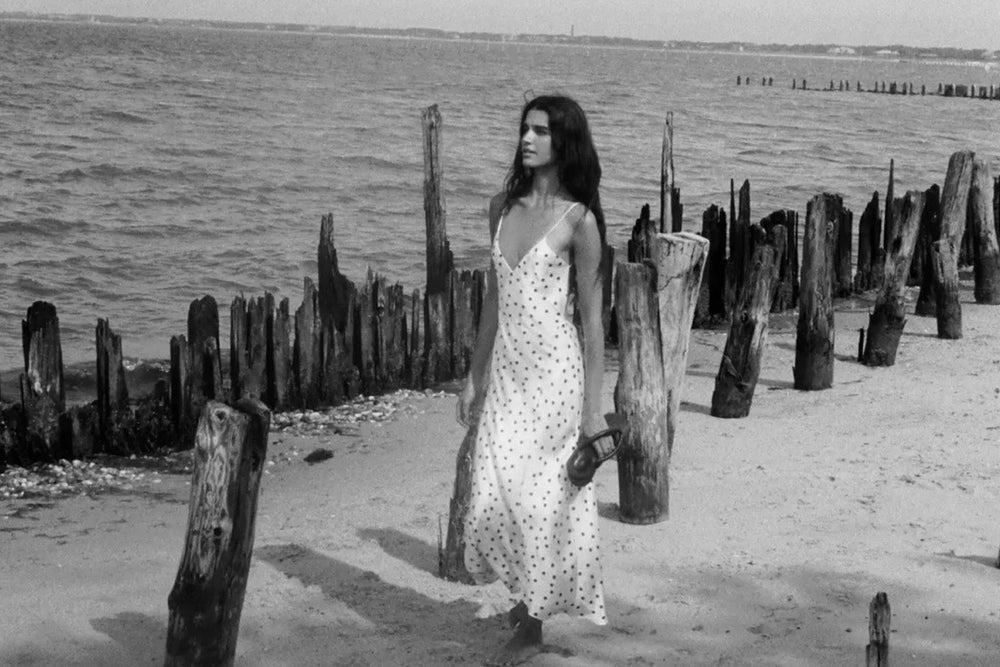 Woman in a long dress standing on a beach with wooden posts in the background