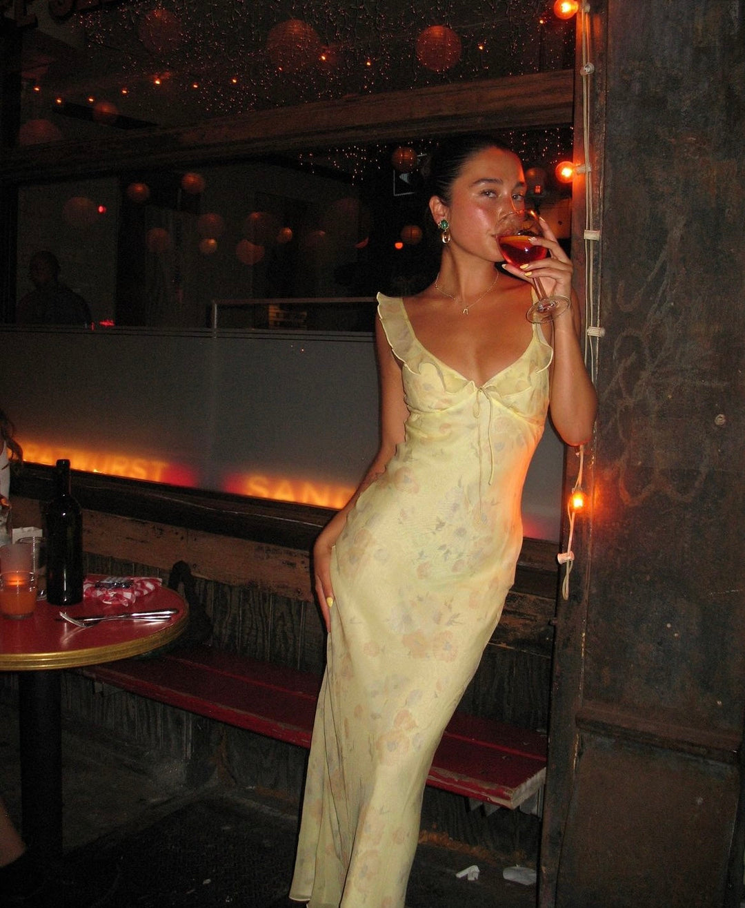 Woman in a yellow dress holding a glass of wine in a dimly lit bar.