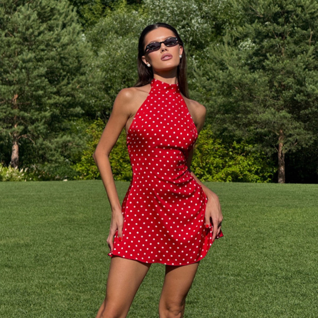 Woman in a red polka dot dress standing on grass with trees in the background