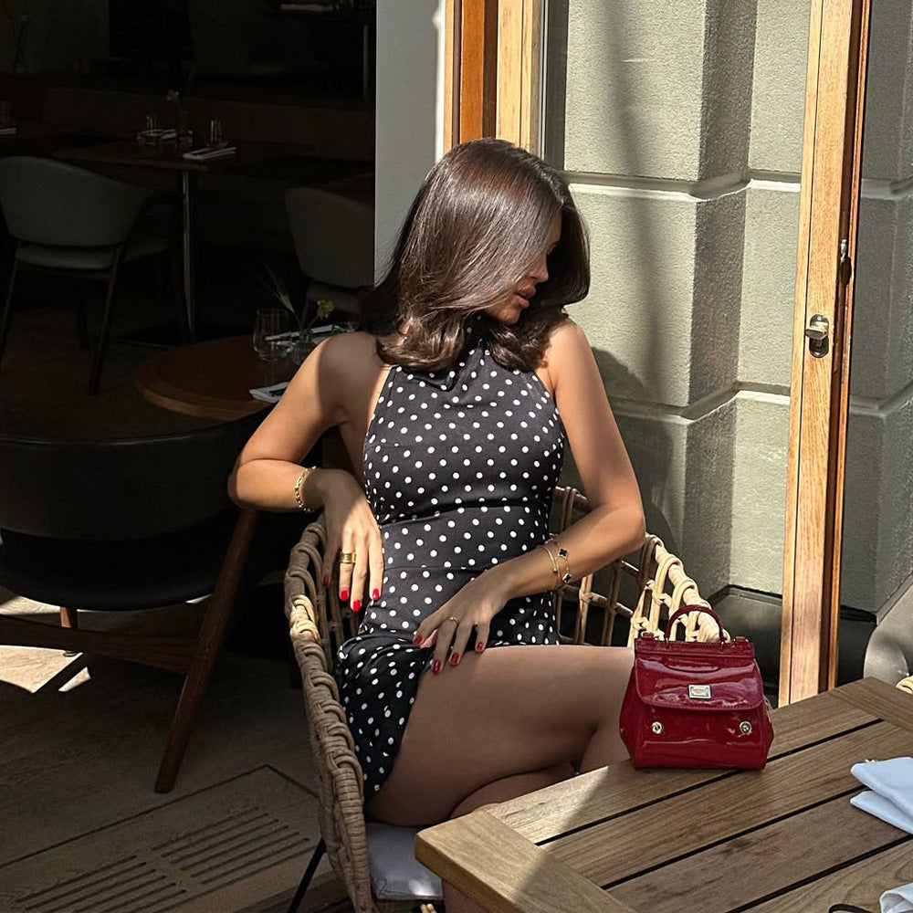 Woman in a polka dot dress sitting at an outdoor cafe table with a red handbag.
