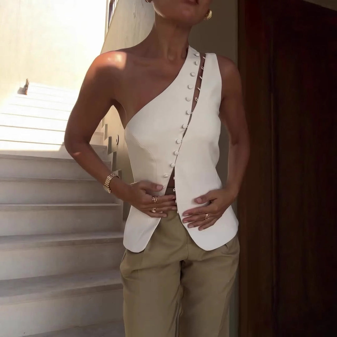 Woman wearing a white one-shoulder top with buttons and beige pants, standing outdoors.