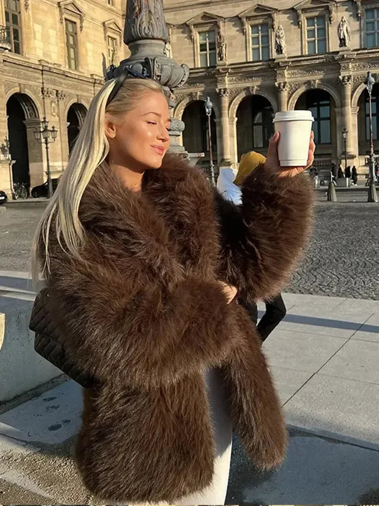 Person wearing a brown fur coat holding a cup in an urban setting.