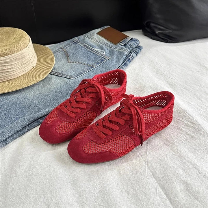 Red sneakers on a white surface with denim jeans and a straw hat in the background.