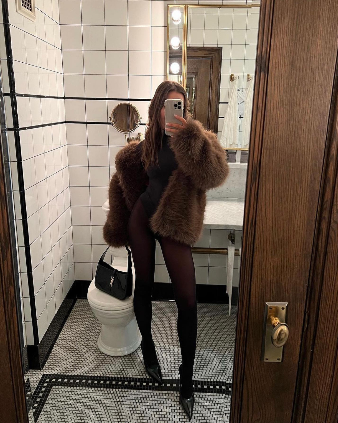 Person taking a mirror selfie in a bathroom wearing a fur coat.