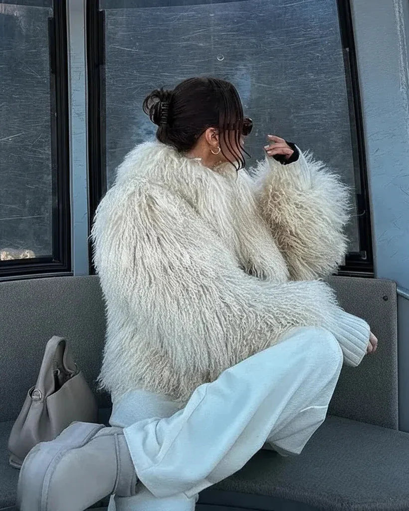 Person wearing a fluffy white coat sitting on a bench.