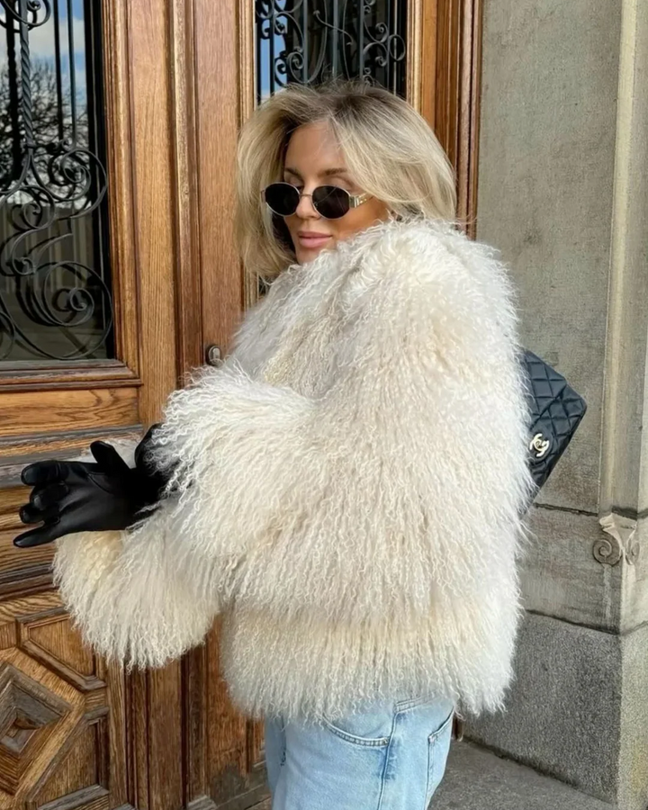 Person wearing a white fluffy coat standing in front of a building entrance.