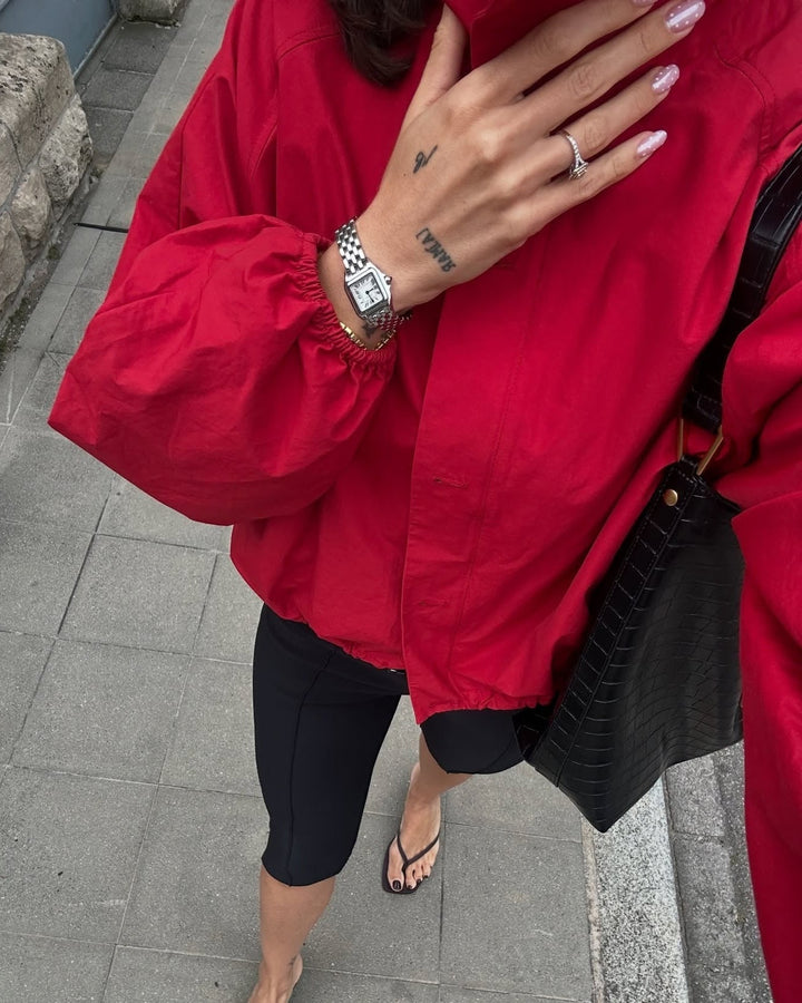 Person wearing a red jacket and black pants on a sidewalk.