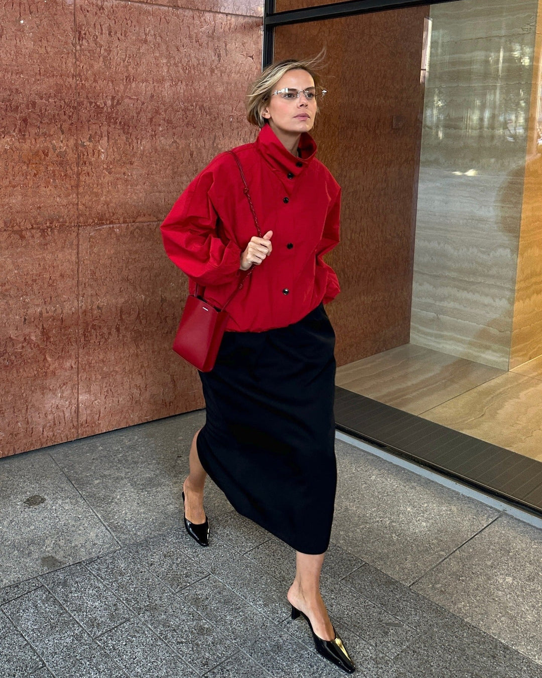 Woman in a red coat and black skirt standing in front of a building entrance.