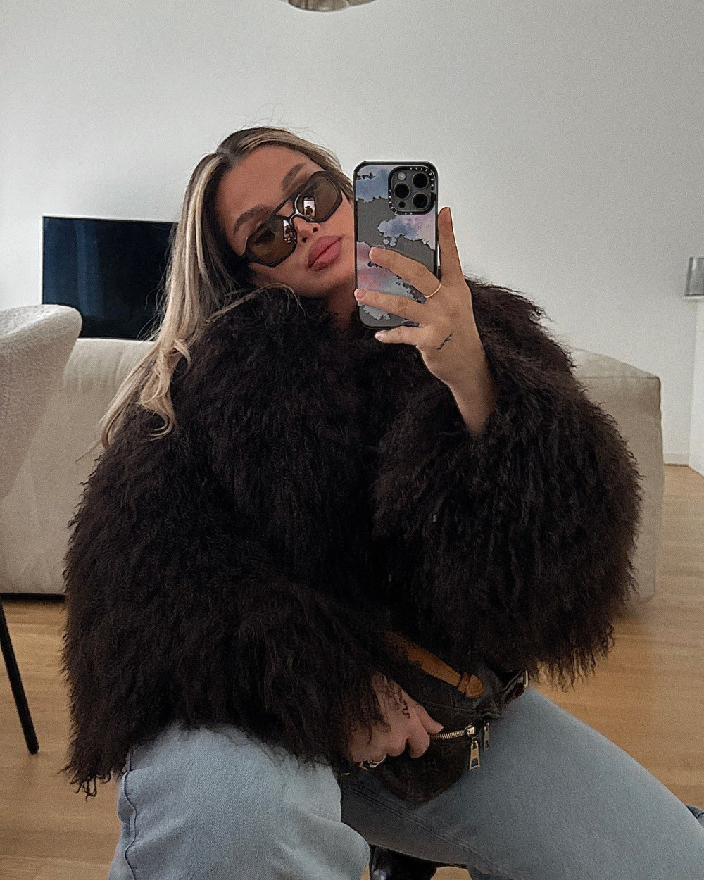 Person wearing a dark brown fluffy coat taking a mirror selfie indoors.