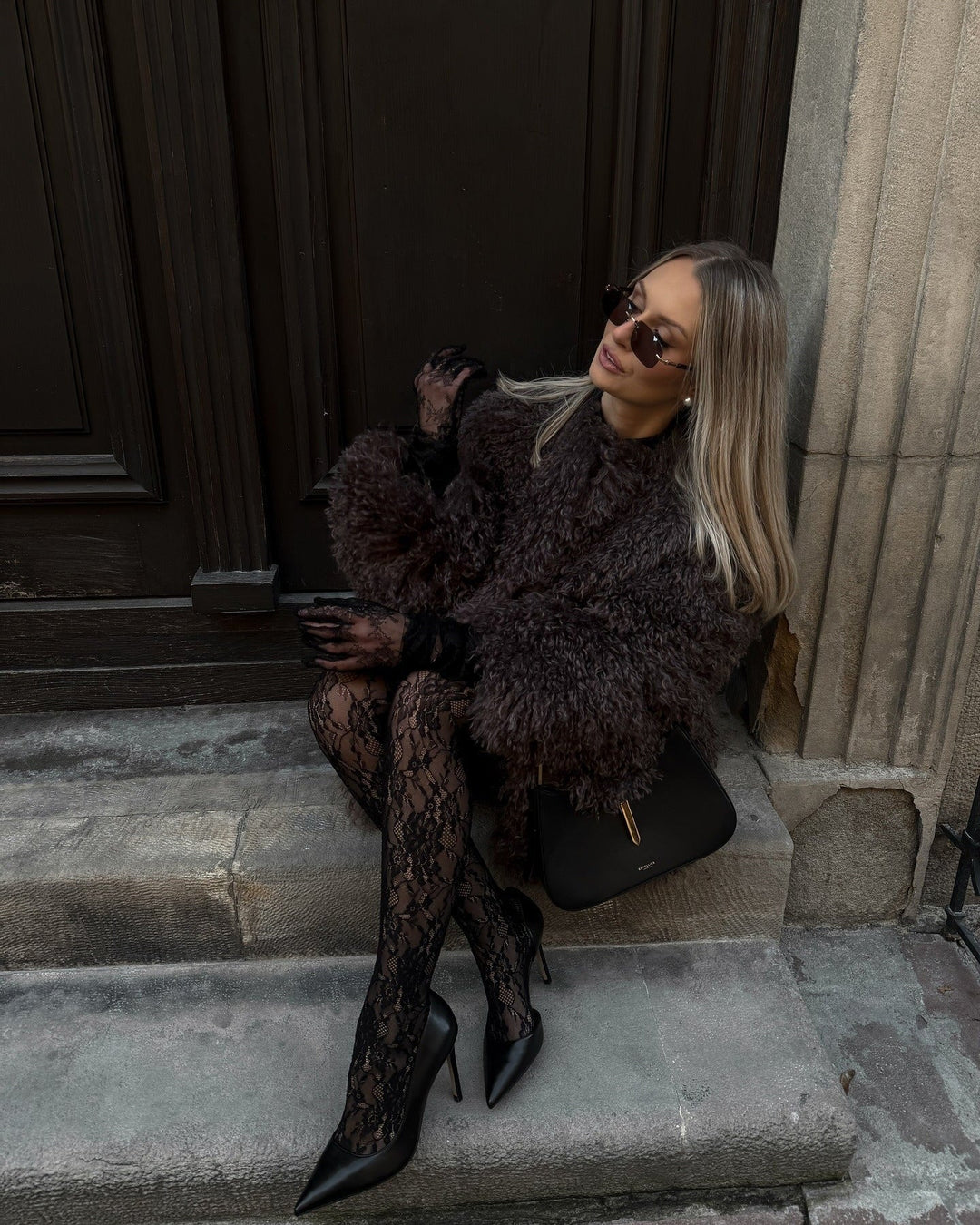 Woman in a dark textured sweater and black lace tights sitting on steps.